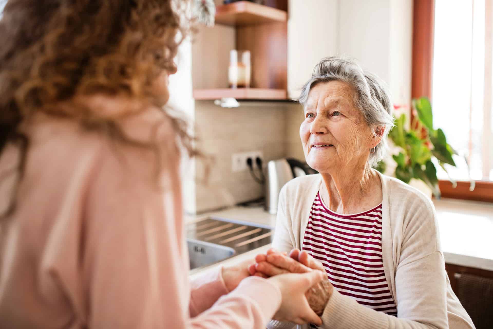 Caregiver gently holding hands with a senior resident in a sunlit kitchen