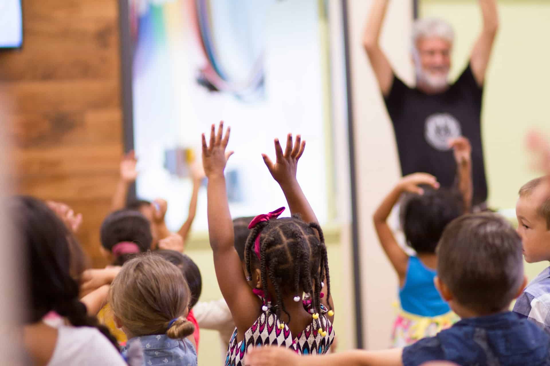 Children and a senior raising hands together during an intergenerational program activity