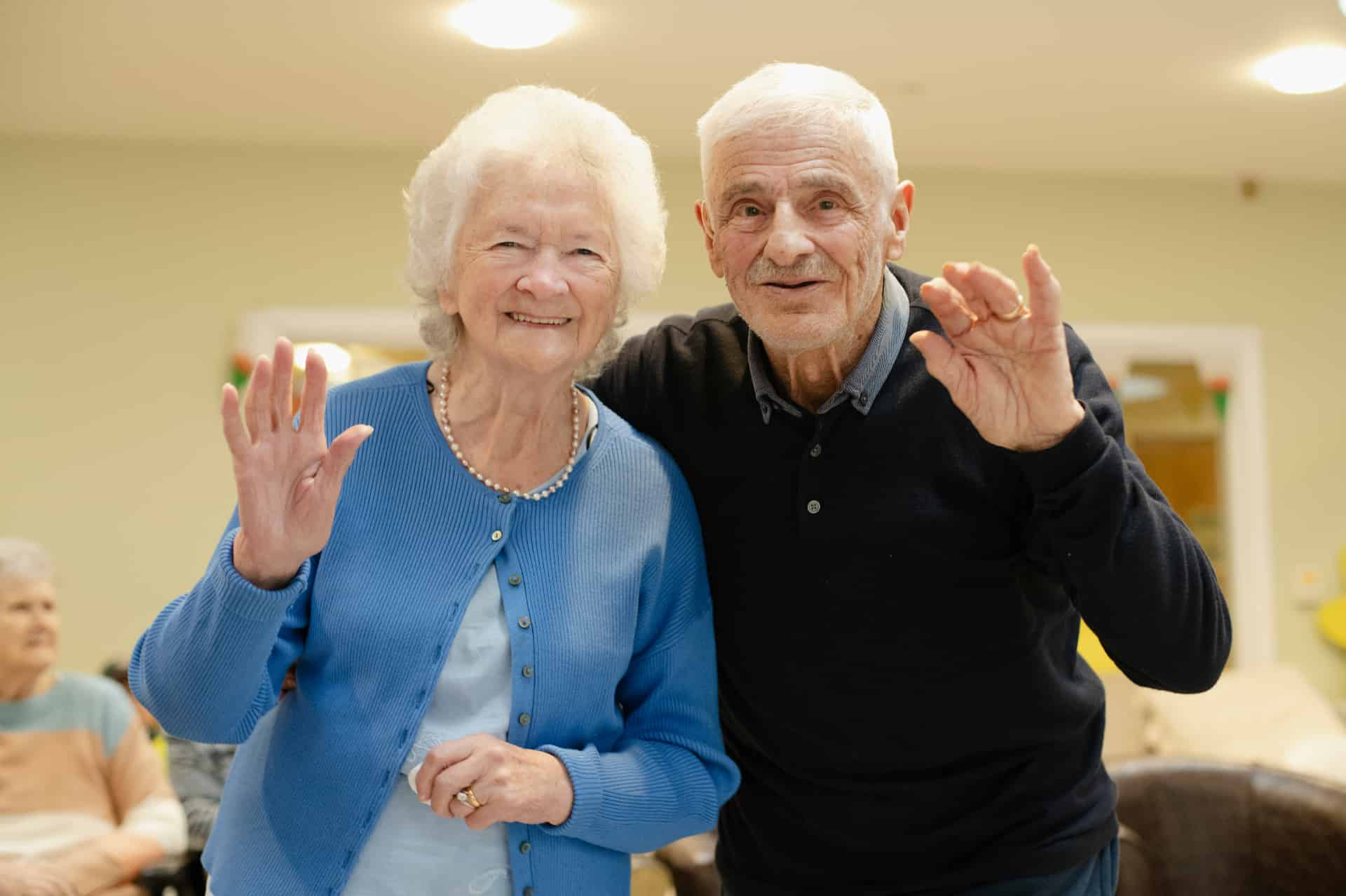 Two cheerful residents waving in a bright activity room