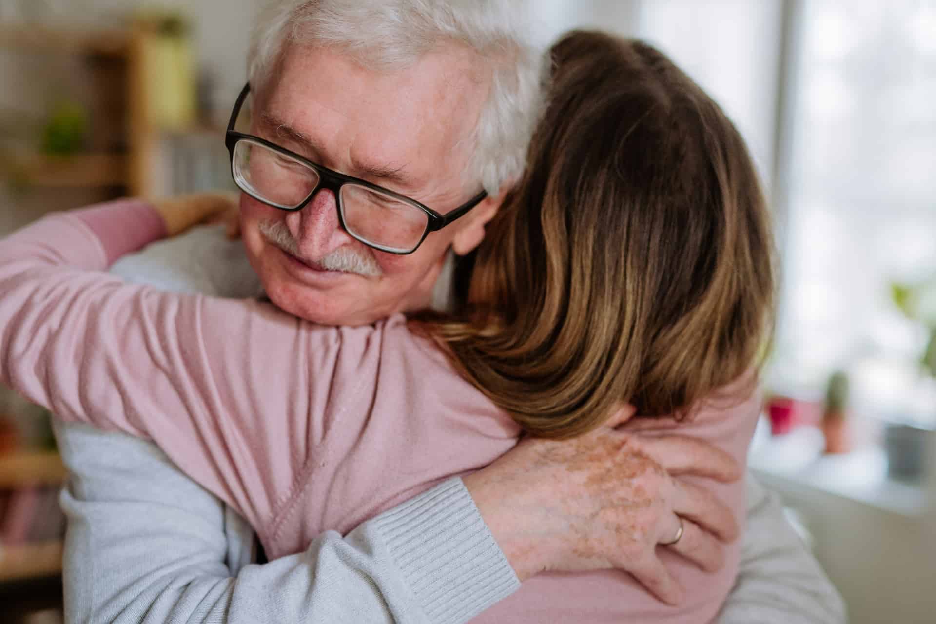 Senior man sharing a warm embrace with a caregiver in a bright home setting
